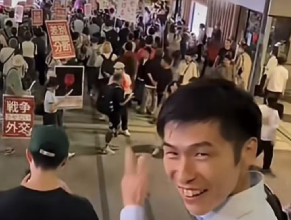 しばき隊の演説妨害を指差しながら笑顔で見ている山添拓氏